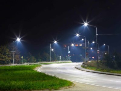 3 A winding road at night is brightly illuminated by multiple streetlights, with residential buildings and trees in the background.
